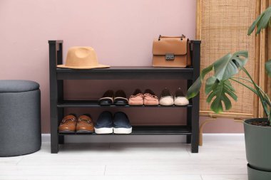 Evin içinde tozlu pembe duvarın yanında farklı ayakkabı ve aksesuarlarla dolu ayakkabı deposu.