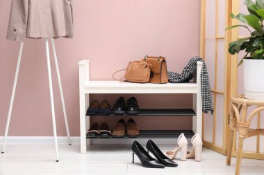 Farklı ayakkabı, aksesuarlar ve kapalı kapılar ardında tozlu pembe duvarın yanında saklama tezgahı.