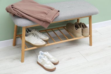 Shoe storage bench with different footwear and clothes near green wall indoors