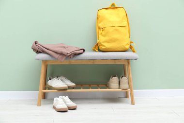 Ayakkabı bankı, farklı ayakkabılar, sırt çantası ve yeşil duvarın yanındaki kıyafetler.