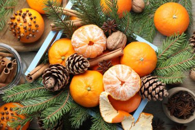 Ripe tangerines, spices, walnuts, fir tree branches and cones in crate on wooden table, flat lay