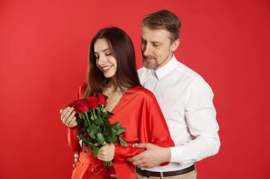 Kırmızı arka planda gül buketi olan mutlu bir çift. Sevgililer Günü kutlaması