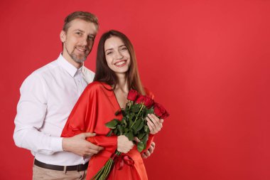 Kırmızı arka planda gül buketi olan mutlu çift, mesaj için yer var. Sevgililer Günü kutlaması