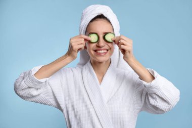 Havluya sarılı güzel bir kadın ve açık mavi arka planda salatalık dilimleri.