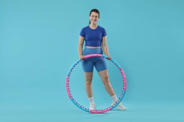 Açık mavi arka planda hula çemberi olan mutlu kadın.