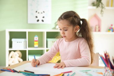 Masada pastel boyayla resim çizen sevimli küçük kız.