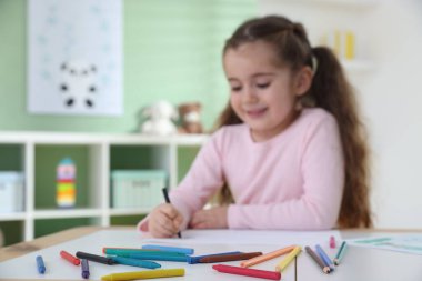 Masada pastel boyayla resim çizen tatlı bir kız. Seçici bir odak noktası.