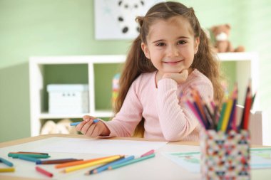 Masada pastel boyayla resim çizen sevimli küçük kız.