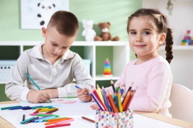 Çocuklar kalem ve pastel boyayla resim çiziyor.