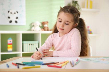 Masada pastel boyayla resim çizen sevimli küçük kız.