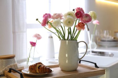 Güzel ranunculus çiçekli ahşap tepsi ve mutfakta taze kruvasan.