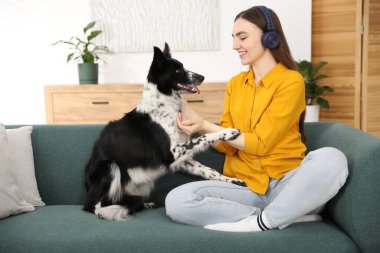 Evdeki kanepede sevimli köpeğiyle kulaklıklı, gülümseyen bir kadın.
