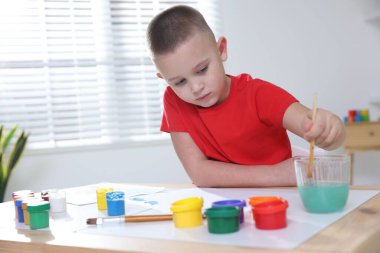Masada fırçayla resim yapan şirin bir çocuk.