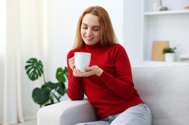 Evdeki kanepede bir fincan aromatik kahveyle güzel bir kadın.