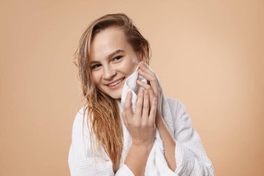 Bej arka planda havluyla saçlarını kurutan güzel bir kadın.