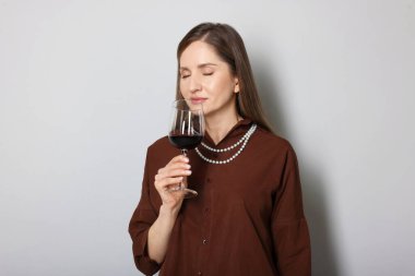 Profesyonel şarap garsonu açık gri arka planda şarap tadıyor.