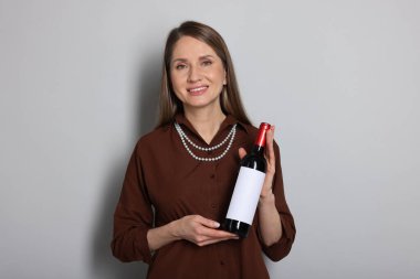 Açık gri arka planda şarap şişesi olan profesyonel şarap garsonu.