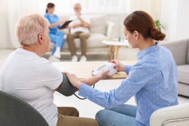 Bakıcı evde yaşlı kadının kan basıncını ölçüyor.