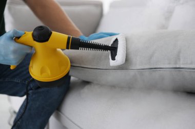 Haşere kontrol işçisi temizlik yastığını içeride buhar temizleyicisiyle temizliyor, yakın plan.