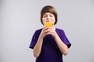 Açık gri arka planda bir bardak taze portakal suyu olan çocuk.