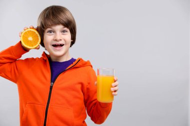 Açık gri arka planda bir bardak taze portakal suyu ve meyveli çocuk. Metin için boşluk