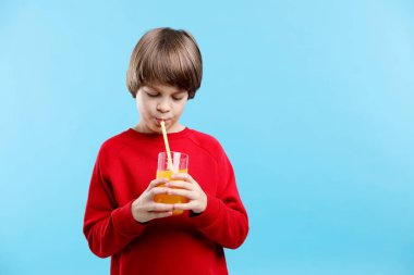 Açık mavi arka planda bir bardak taze portakal suyu olan çocuk. Metin için boşluk
