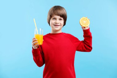 Açık mavi arka planda taze portakal suyu ve meyvesi olan bir çocuk.