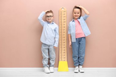 Küçük çocuk ve kız bej duvarın yanında boylarını grafikle ölçüyorlar.