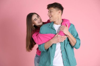 Mutlu çift pembe arka planda birbirlerine sarılıyorlar.