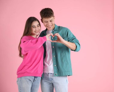 Mutlu çift pembe arka planda kalp hareketi yapıyor.