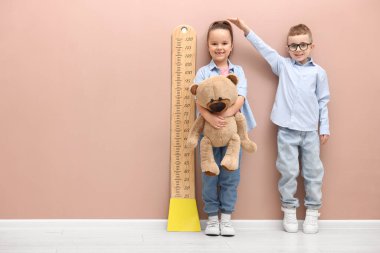 Küçük çocuk ve kız bej duvarın yanında boylarını grafikle ölçüyorlar. Metin için boşluk