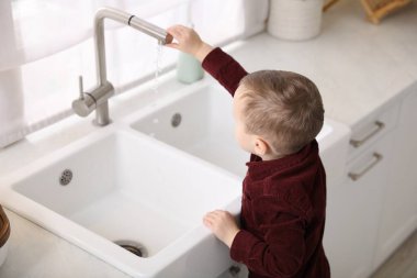 Evde çocuk güvenliği. Küçük çocuk mutfakta lavabo açıyor.