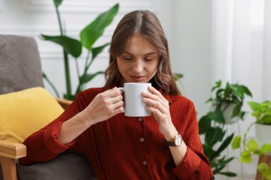 Evdeki koltukta bir fincan aromatik kahveli kadın.