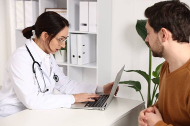 Klinikteki beyaz masada hastayla çalışan bir doktor.