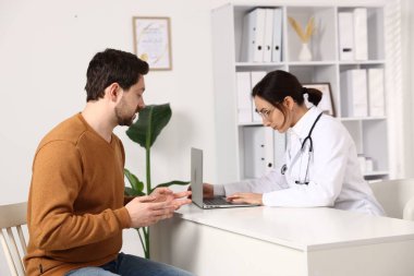 Klinikteki beyaz masada hastayla çalışan bir doktor.