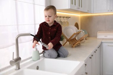 Evde çocuk güvenliği. Küçük çocuk mutfaktaki musluk hortumunu çekiyor.