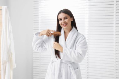 Banyoda saçını tarayan bornozlu bir kadın.