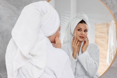 İçerideki aynanın yanındaki havluya sarılmış saçları olan kadın.