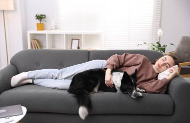 Evdeki kanepede uyuyan sevimli köpeğiyle genç bir kadın.