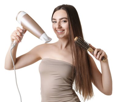 Gülümseyen kadın saçını saç kurutma makinesiyle şekillendiriyor ve beyaz arka planda tarıyor.