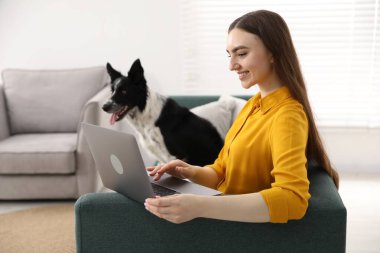 Evdeki kanepede dizüstü bilgisayarı ve sevimli köpeğiyle gülümseyen kadın.