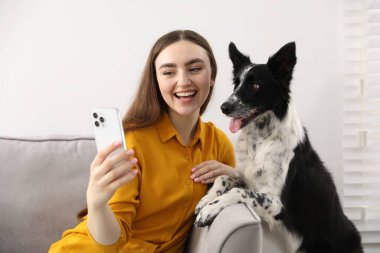 Sevimli köpeğiyle gülümseyen kadın evdeki kanepede selfie çekiyor.