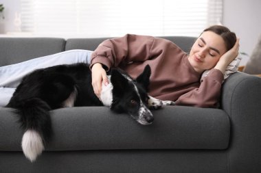 Evdeki kanepede sevimli köpeğiyle yatan genç bir kadın.