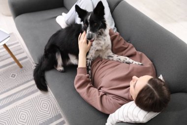 Evdeki kanepede sevimli köpeğiyle yatan bir kadın.