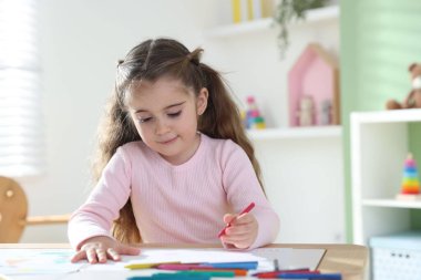 Masada pastel boyayla resim çizen sevimli küçük kız.