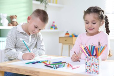 Çocuklar kalem ve pastel boyayla resim çiziyor.
