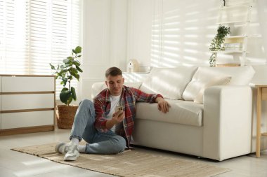 Akıllı telefonlu genç adam evde kanepenin yanında dinleniyor.