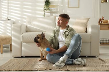 Evdeki kanepenin yanında sevimli köpeği ve oyuncağıyla genç bir adam.