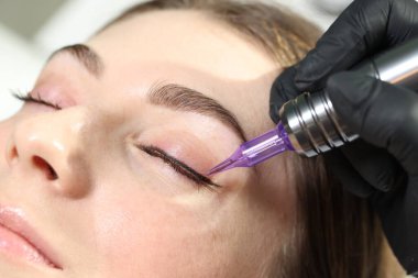 Güzellik uzmanı genç bir kadına kalıcı göz kalemi makyajı yapıyor.