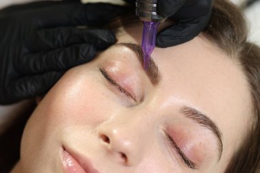 Güzellik uzmanı, genç bayana kalıcı kaş makyajı yapıyor.